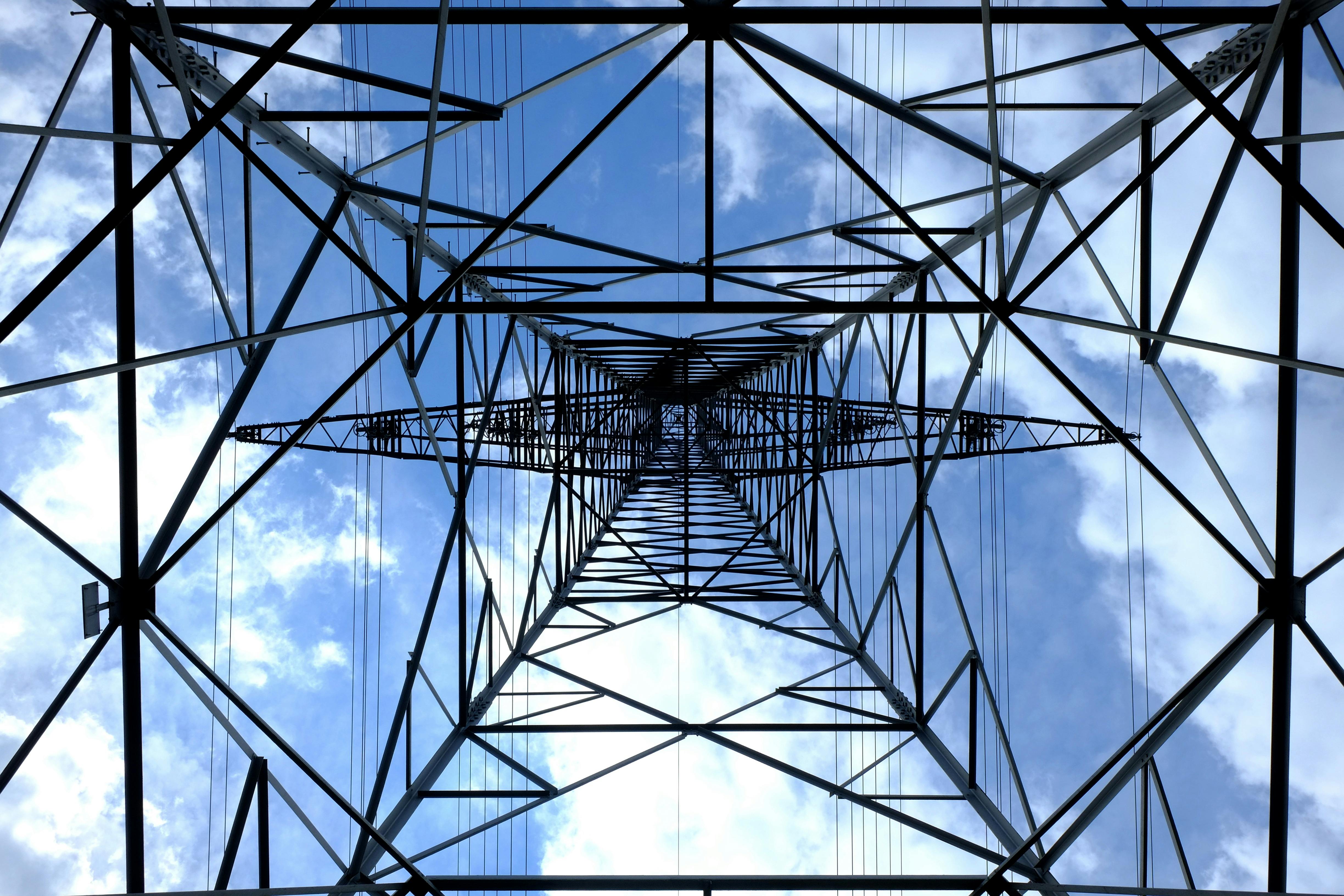 Looking up at a steel power pylon against a bright blue sky.