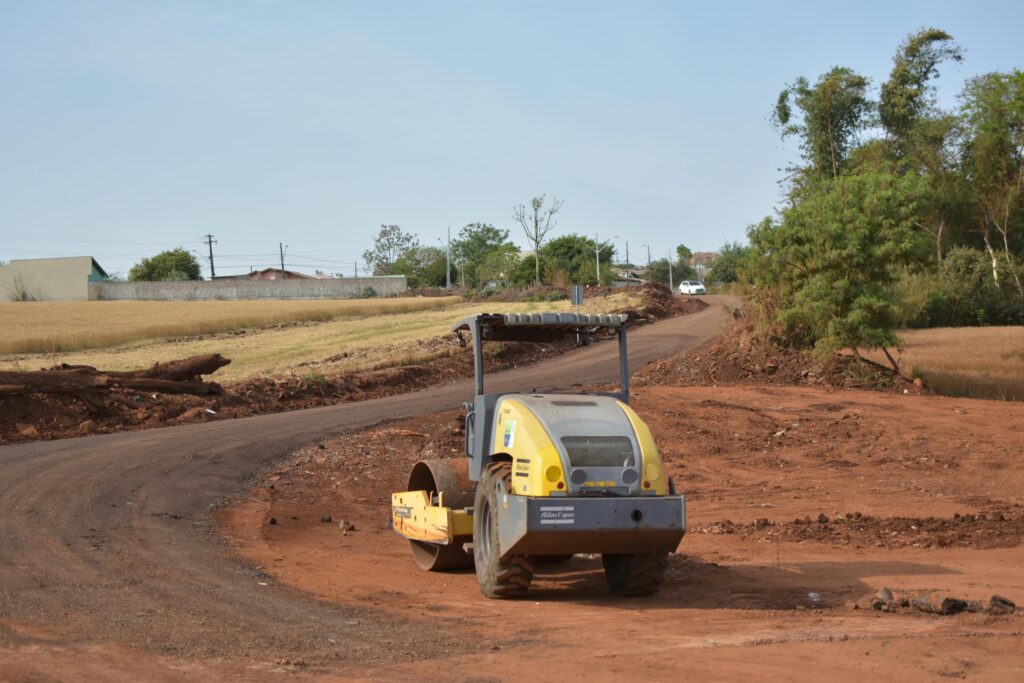 Industrial scene with construction equipment on a dirt road surrounded by fields.